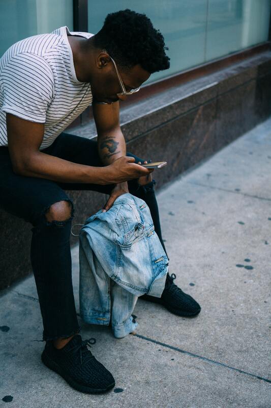 Man sitting on sidewalk holding jacket and using mobile device